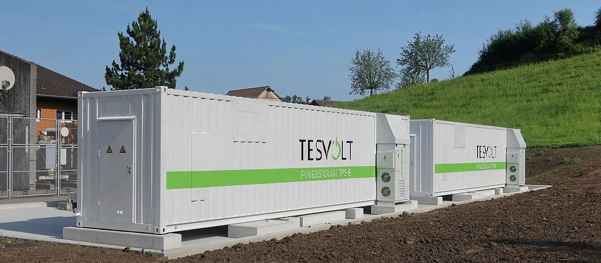 Kontenerowe magazyny energii stojące na fundamencie obok budynków